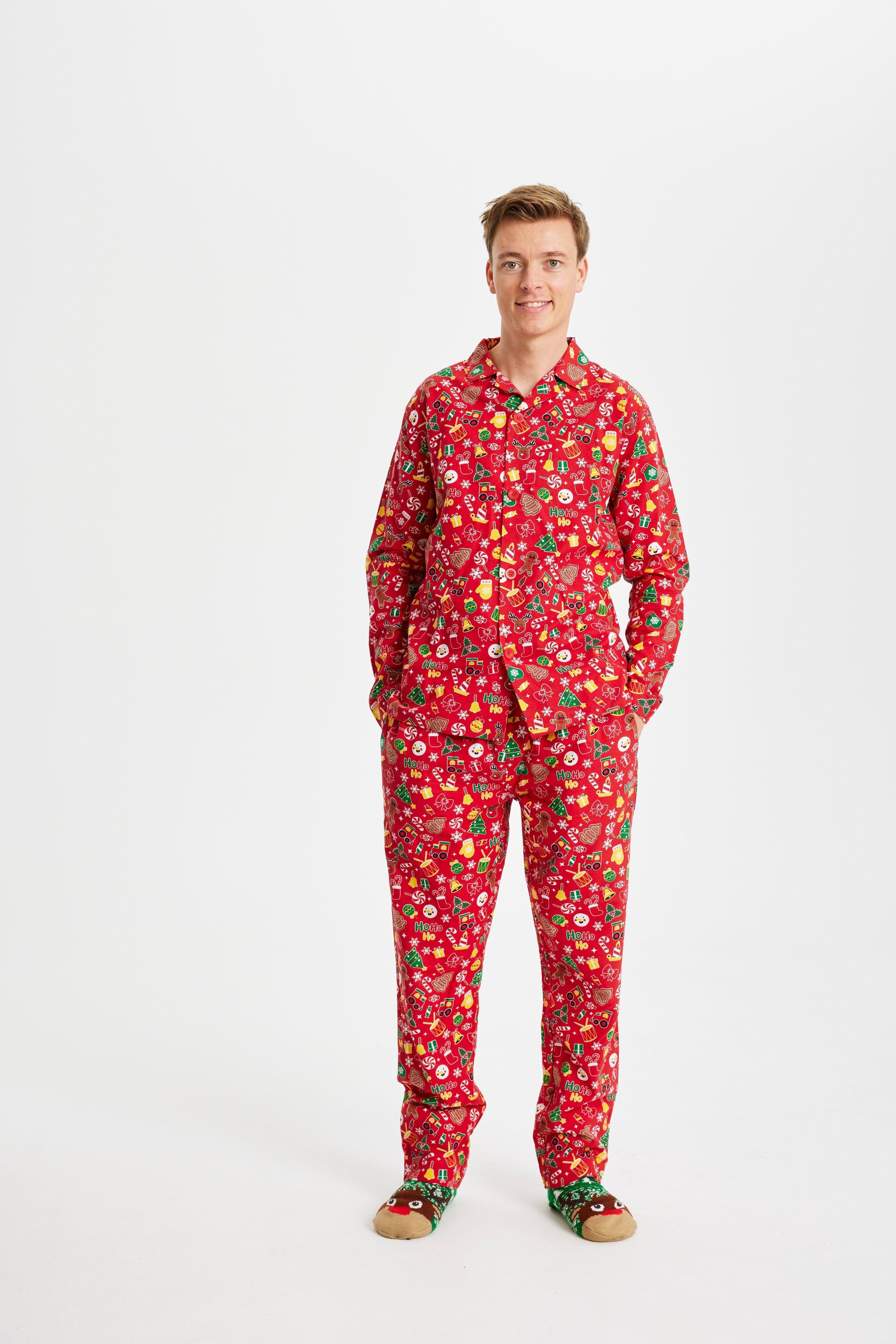 En smilende mand står i julesokker og en rød pyjamas i to dele med julemønster på.